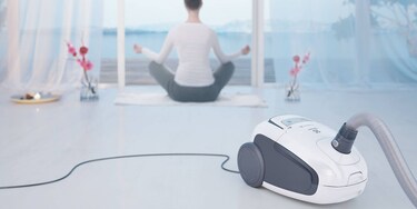 Une femme faisant du yoga avec son aspirateur Ultra Silencer d'Electrolux au premier plan