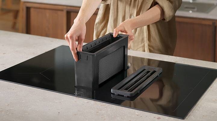 Les mains remettent en place le filtre à graisse d'un extracteur.