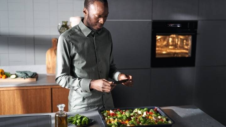 Un homme regardant son téléphone et cuisinant des légumes sur une plaque de cuisson