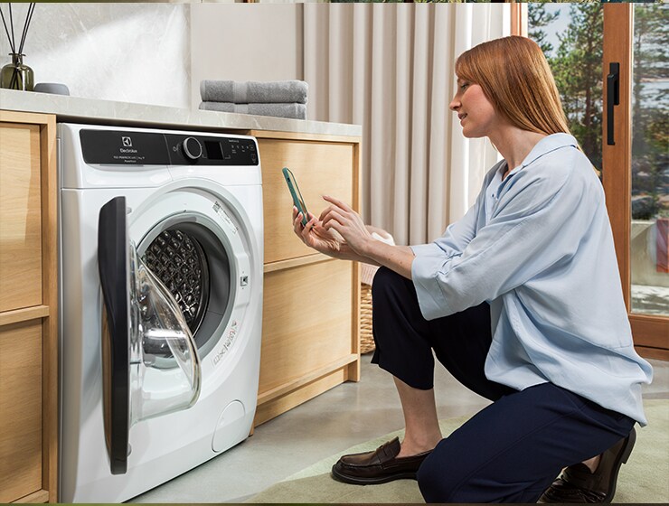 Woman holding a phone in front of washing machine