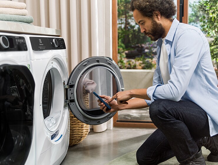 Man holding phone in front of open washing machine