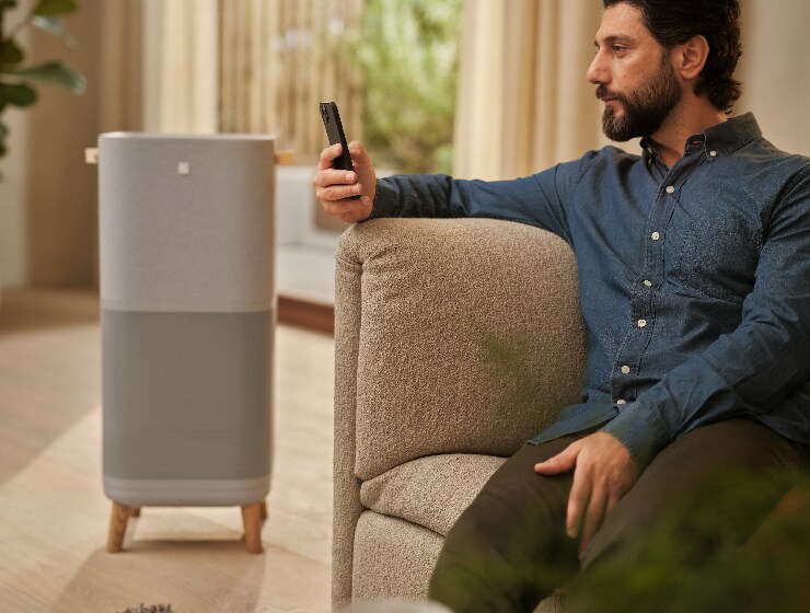 Un homme tenant un téléphone, assis à côté d’un purificateur d’air.