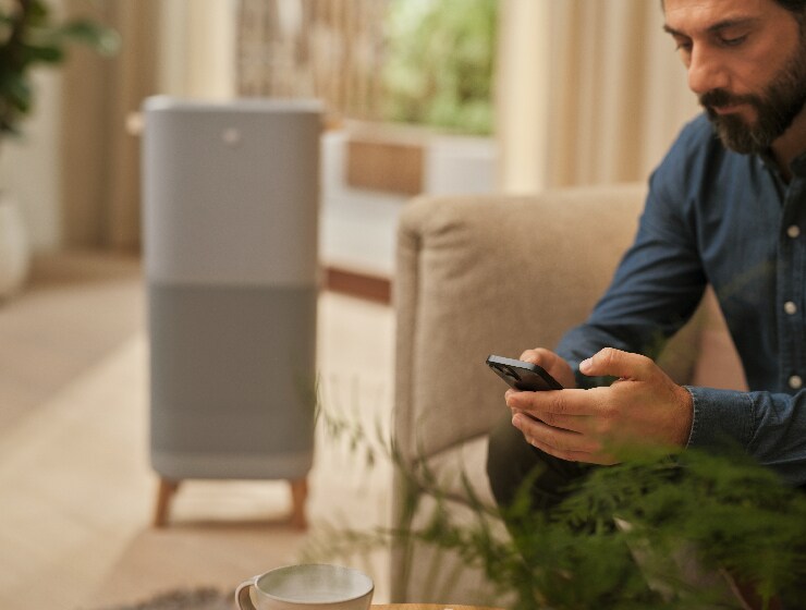Un homme tenant un téléphone, assis à côté d’un purificateur d’air.