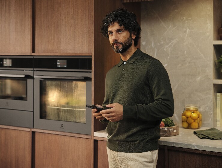 Un homme debout dans la cuisine tenant un téléphone.