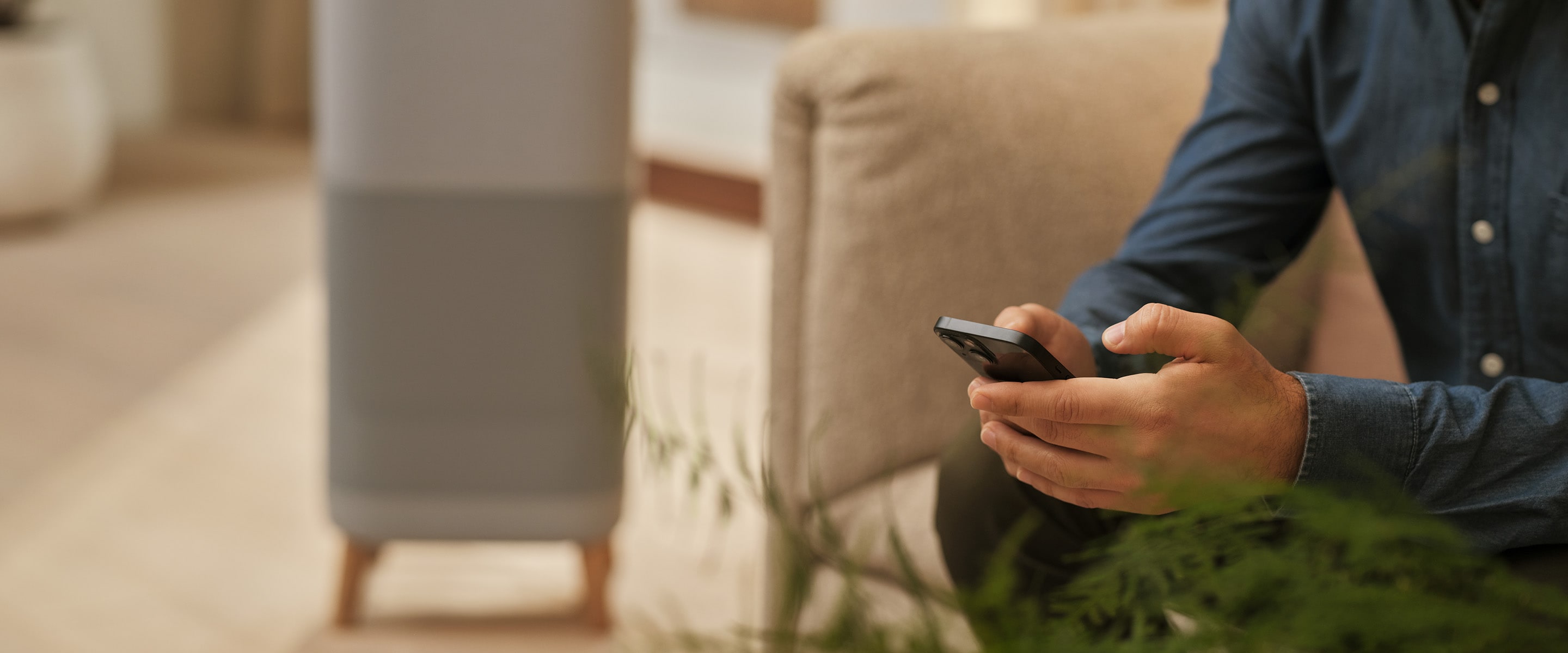 Un homme assis tenant un téléphone. Un purificateur d’air en arrière-plan.